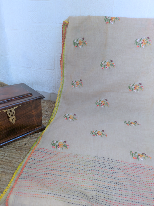 Close-up of a natural beige linen saree showing detailed hand embroidery and multicolored striped pallu with tassels.